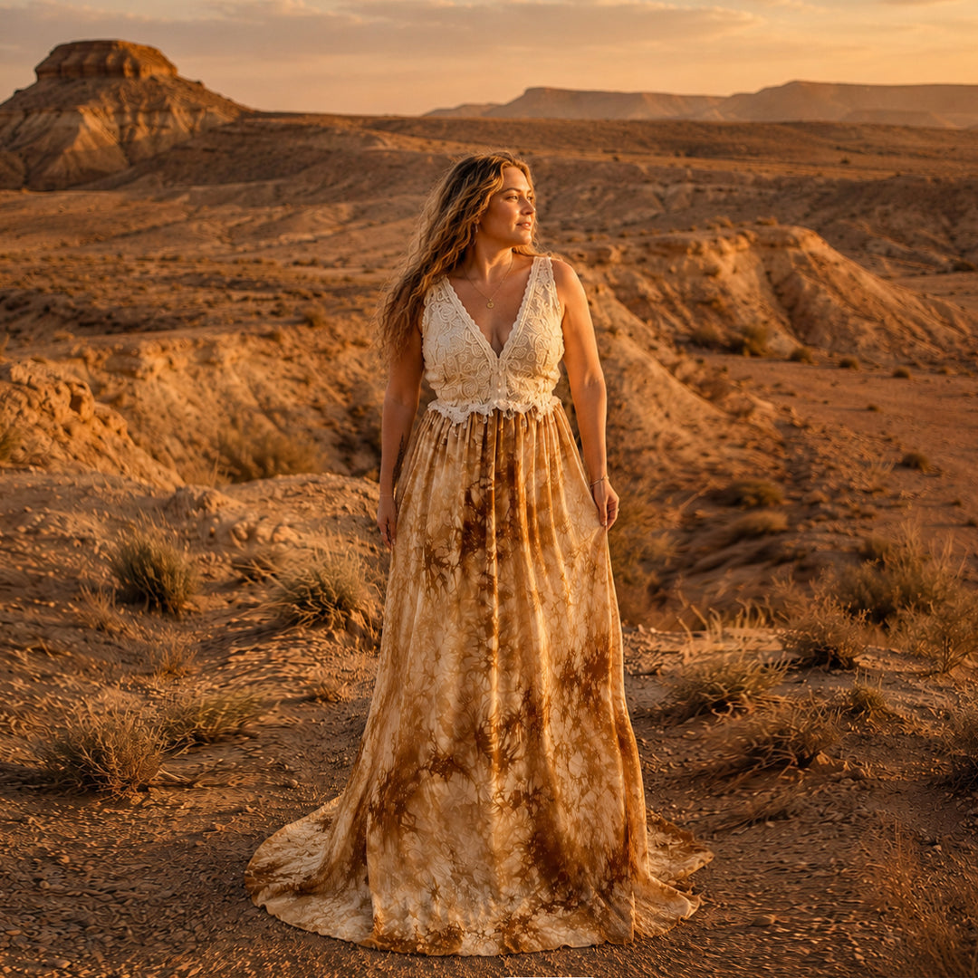 A woman stands in a desert landscape wearing an Aura tie-dye gown with a white crochet top.
