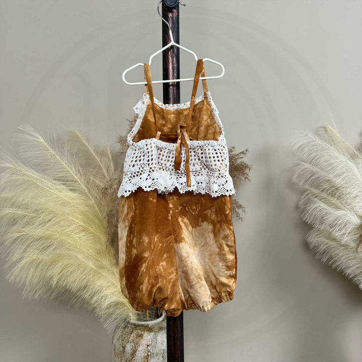 A hanger displays a back view of a Brizo coffee tie-dye romper with a white lace top.