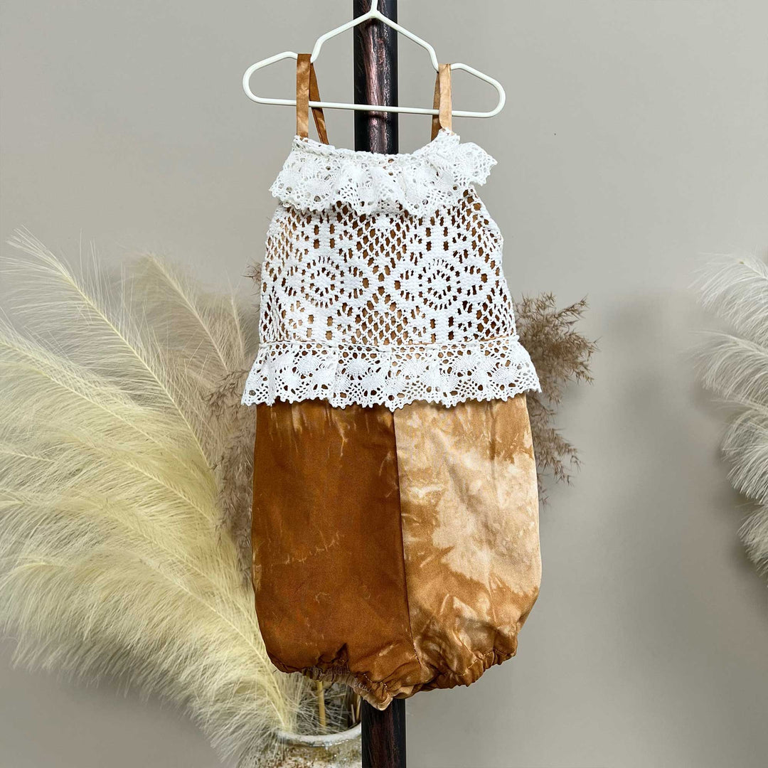 A hanger displays a Brizo coffee tie-dye romper with a white lace top.