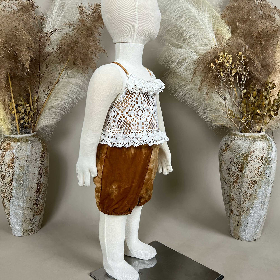 A mannequin displays a side view of a Brizo coffee tie-dye romper with a white lace top.