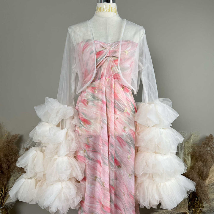A mannequin displays a Eileithyia pink printed strapless dress with a light apricot  sheer bolero and tiered sleeves; the dress features pleats.
