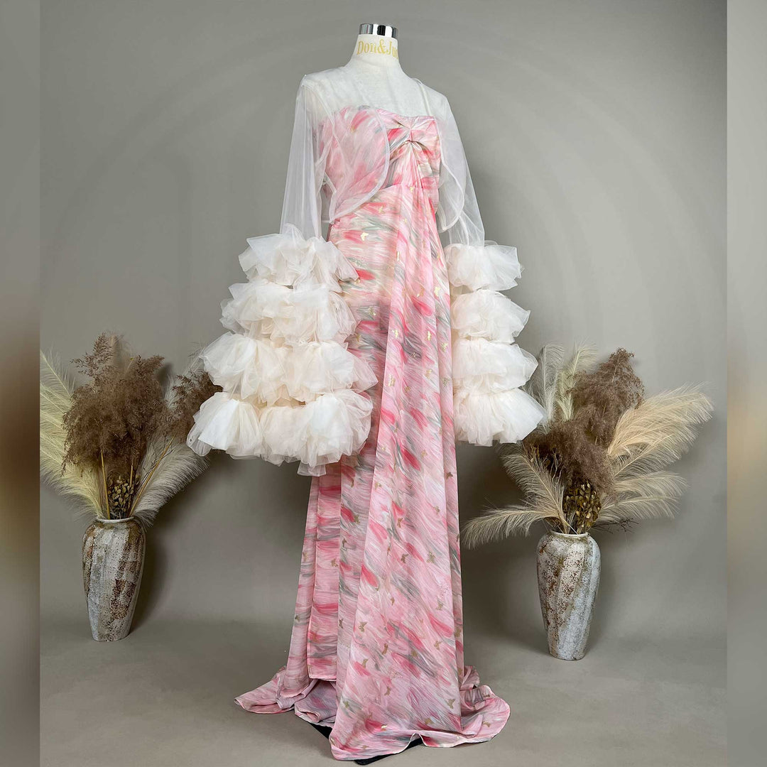 A mannequin displays a side view of a Eileithyia pink printed strapless gown with a light apricot sheer bolero and tiered cuffs; the dress features a train.