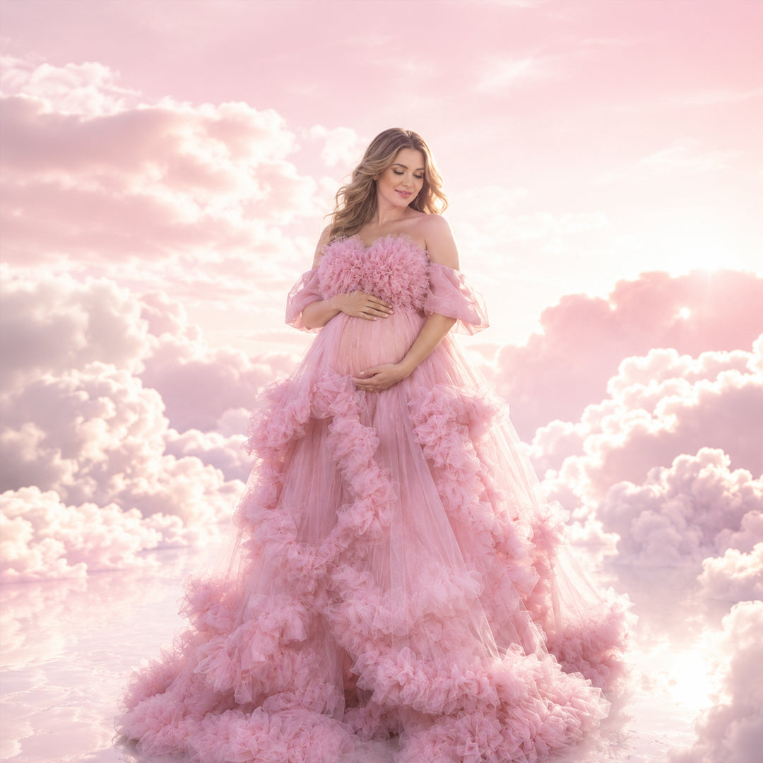 A pregnant woman stands in a Electra pink off-shoulder ruffled gown, holding her belly; the dress features multi-layered ruffles.