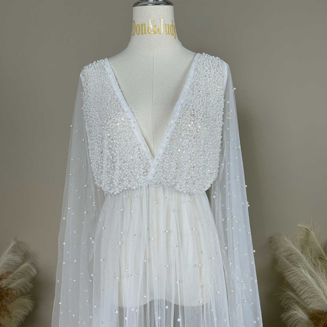 A mannequin displays a Eos ivory deep-V beaded top with sheer long sleeves; the bodice and sleeves feature pearl embellishments.