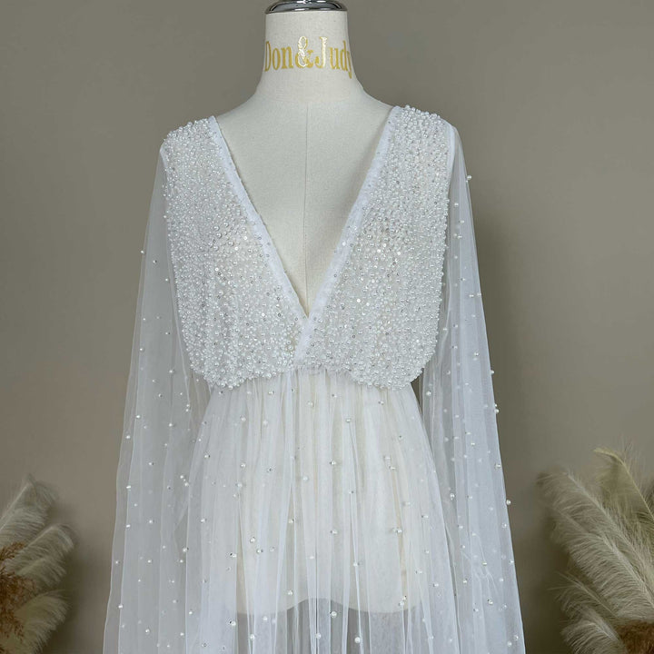 A mannequin displays a Eos ivory deep-V beaded top with sheer long sleeves; the bodice and sleeves feature pearl embellishments.