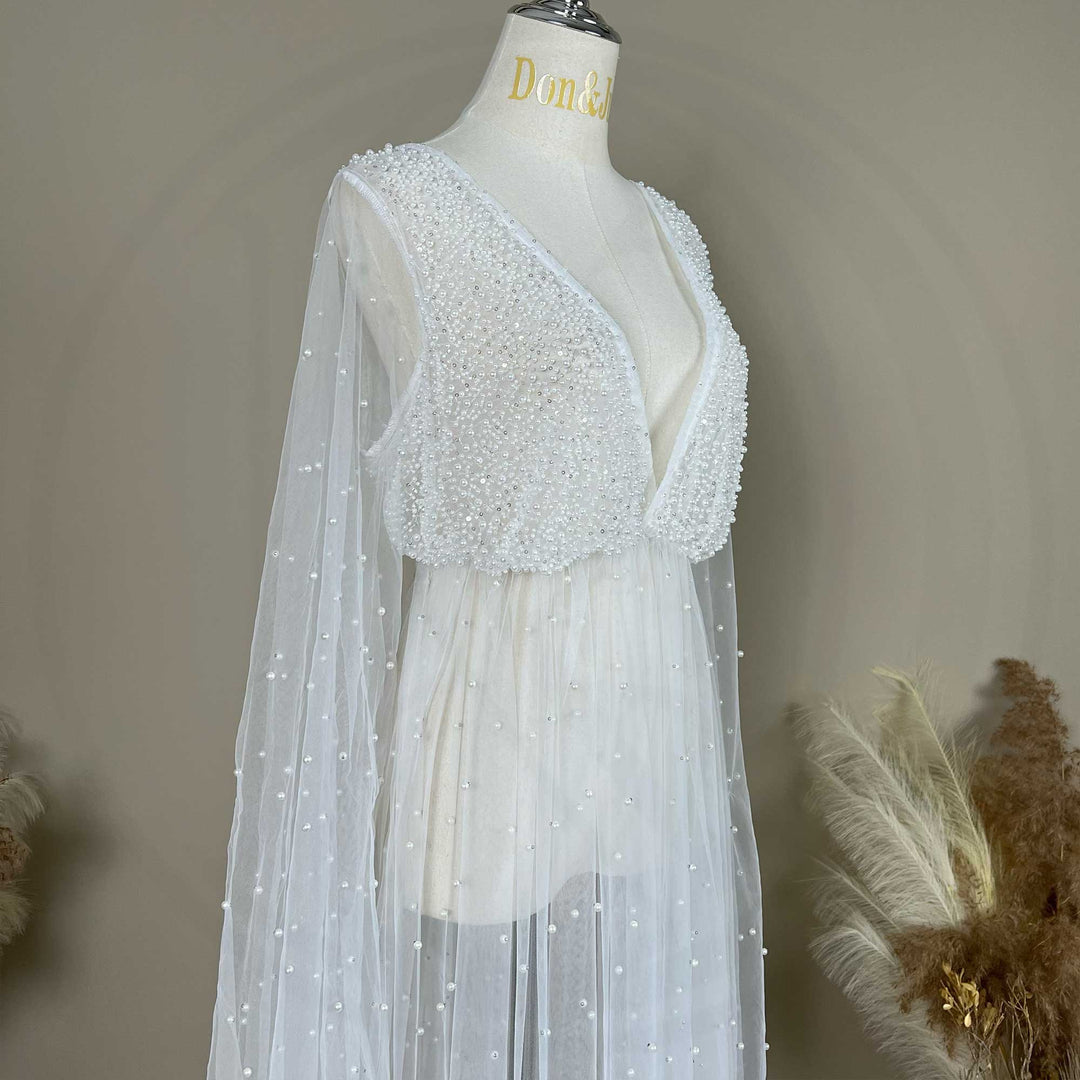 A close up of a Eos ivory deep-V beaded bodysuit with a sheer skirt; the dress features lantern sleeves and pearl embellishments.