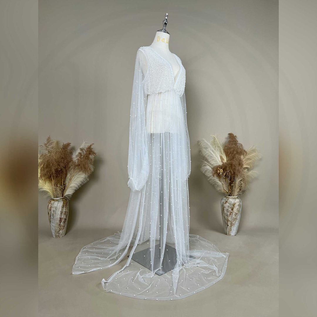 A mannequin show a side view of a Eos ivory deep-V beaded bodysuit with a sheer skirt; the dress features lantern sleeves and pearl embellishments.
