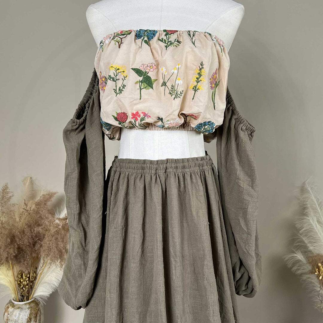 Close up of a mannequin displays a Freda floral top, solid skirt, and detached sleeves.