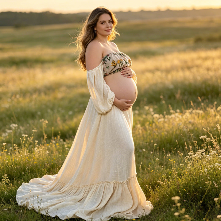 A pregnant woman stands sideways in a field wearing a Freda beige boho embroidery floral two-piece dress, holding her belly.The background is grass and wildflowers,
