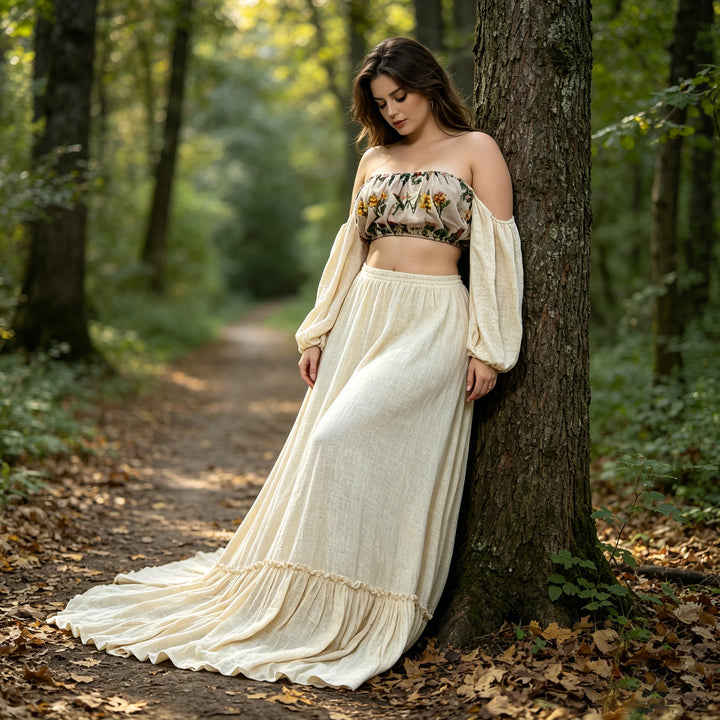A woman wearing a Freda beige floral tube top and beige skirt leans against a tree trunk in a forest.