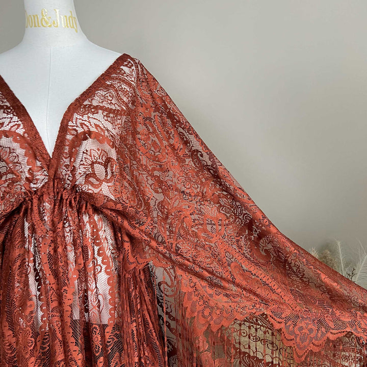 A mannequin displays a close-up of a  Hemera terracotta lace cape featuring floral openwork texture and a deep V-neck; the fabric is semi-transparent mesh.