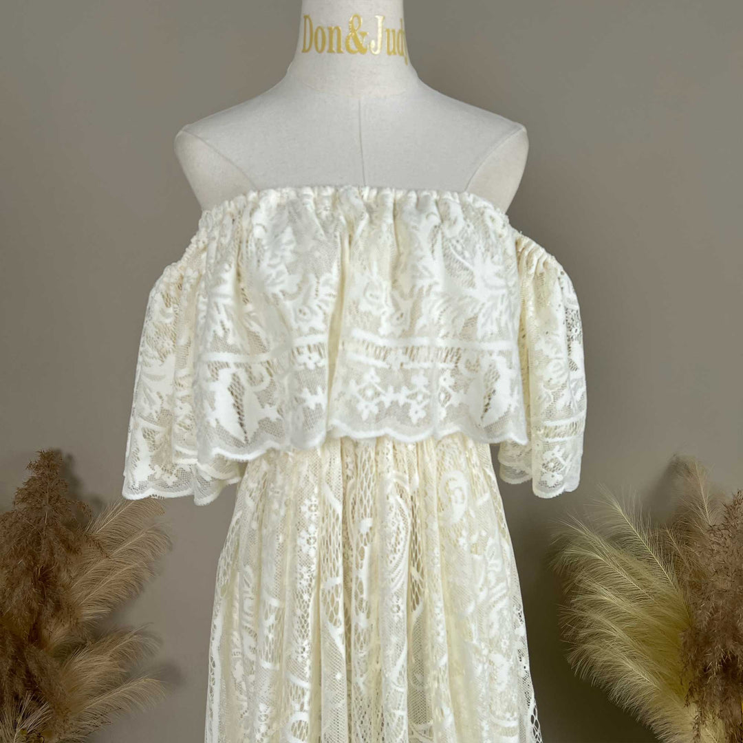 A mannequin displays the upper body of a Kymopoleia beige off-shoulder lace gown with ruffled sleeves and a train.