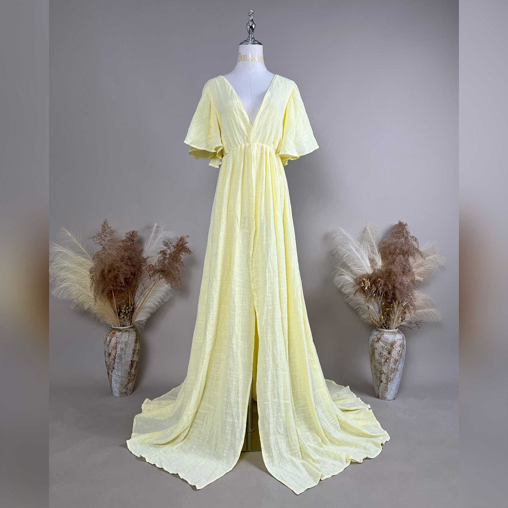 A mannequin displays a Megaera yellow V-neck short-sleeve gown with a high-waist pleat and train; the fabric has a textured finish.
