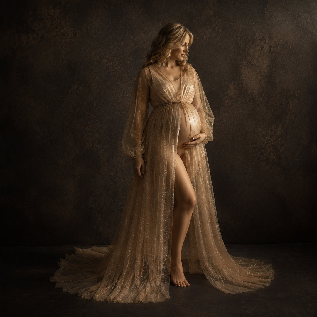 A pregnant model in a Metis khaki sequined V-neck robe stands against a dark background, wearing a light bodysuit underneath with one hand on her belly; the robe features lantern sleeves, a tie belt, and a floor-length train.