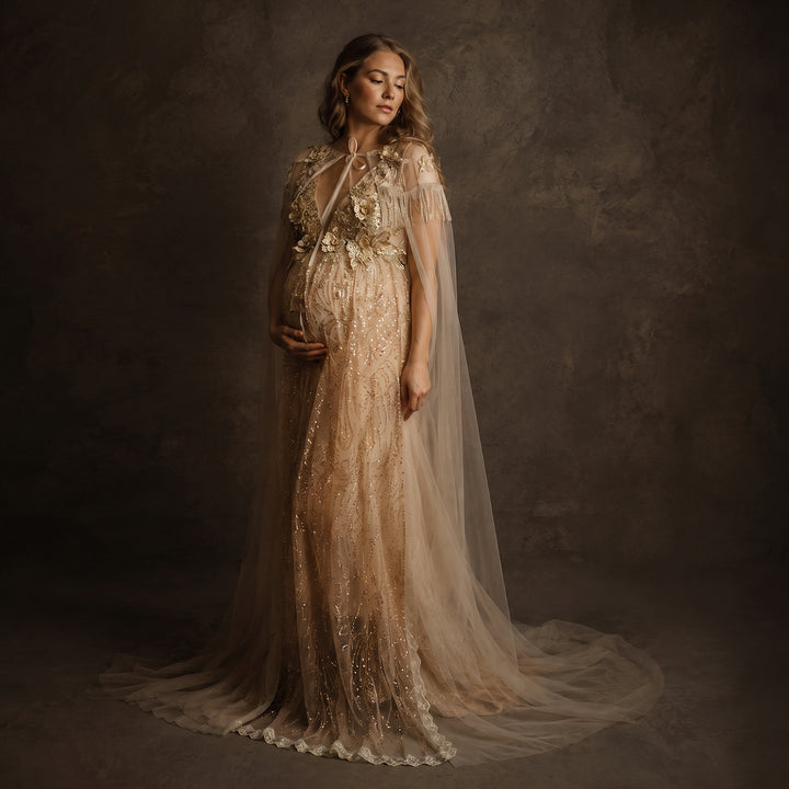 A pregnant model displays a Pandia gold sequined gown with a tulle cape, featuring 3D floral decorations and a train skirt.