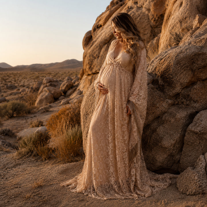 A pregnant woman in a Pheme  khaki lace fringe gown stands beside desert boulders, one hand on belly.